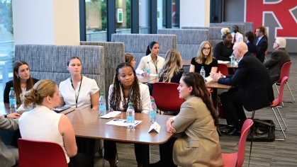 A photo of a networking event taking place. Three tables are lined up with different groups of people talking to a mentor in on of the Rutgers lounges.